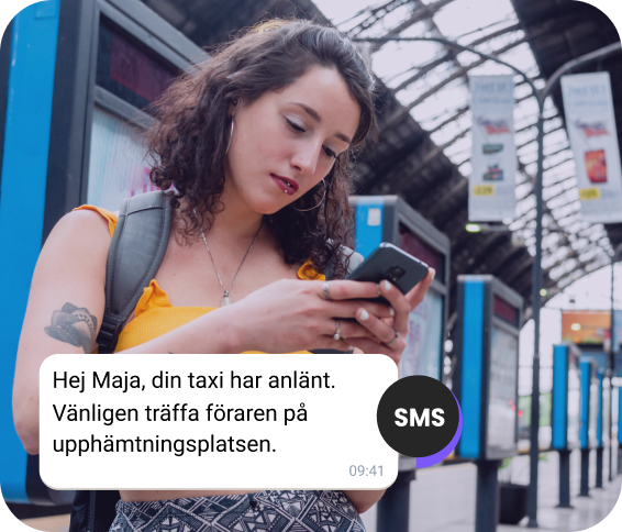 Tjej med ryggsäck på stationen kollar ett SMS om hennes taxi som är på väg